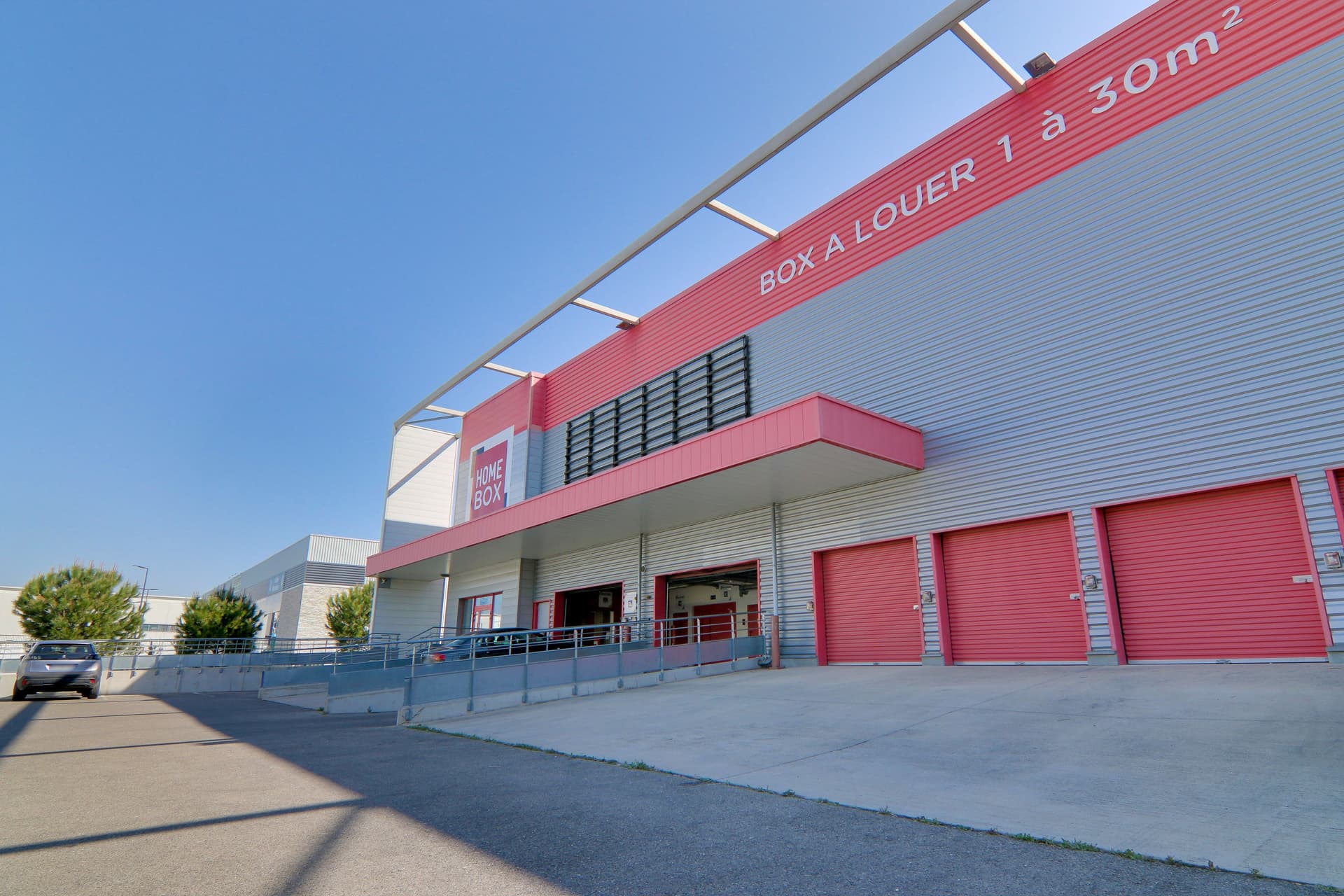Vue latérale du bâtiment avec rideaux rouges et signalétique box à louer, HOMEBOX Nîmes, Place André Bazile, Zac du Mas de Vignolles à Nîmes