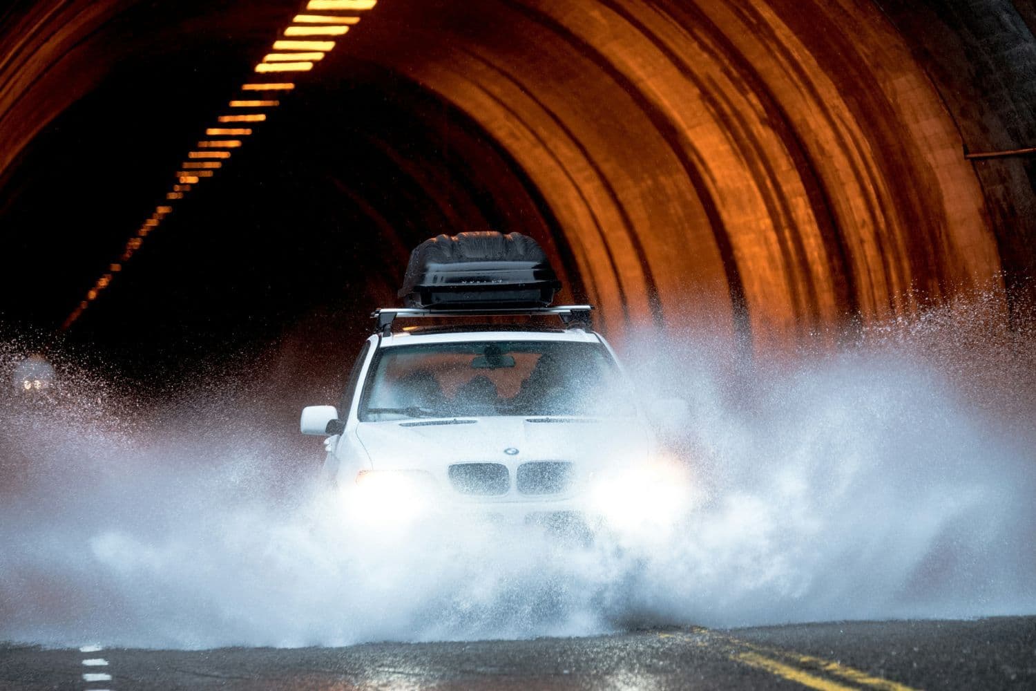 BMW blanche dotée d’un coffre de toit noir sortant d’un tunnel en roulant dans une vaste flaque d’eau