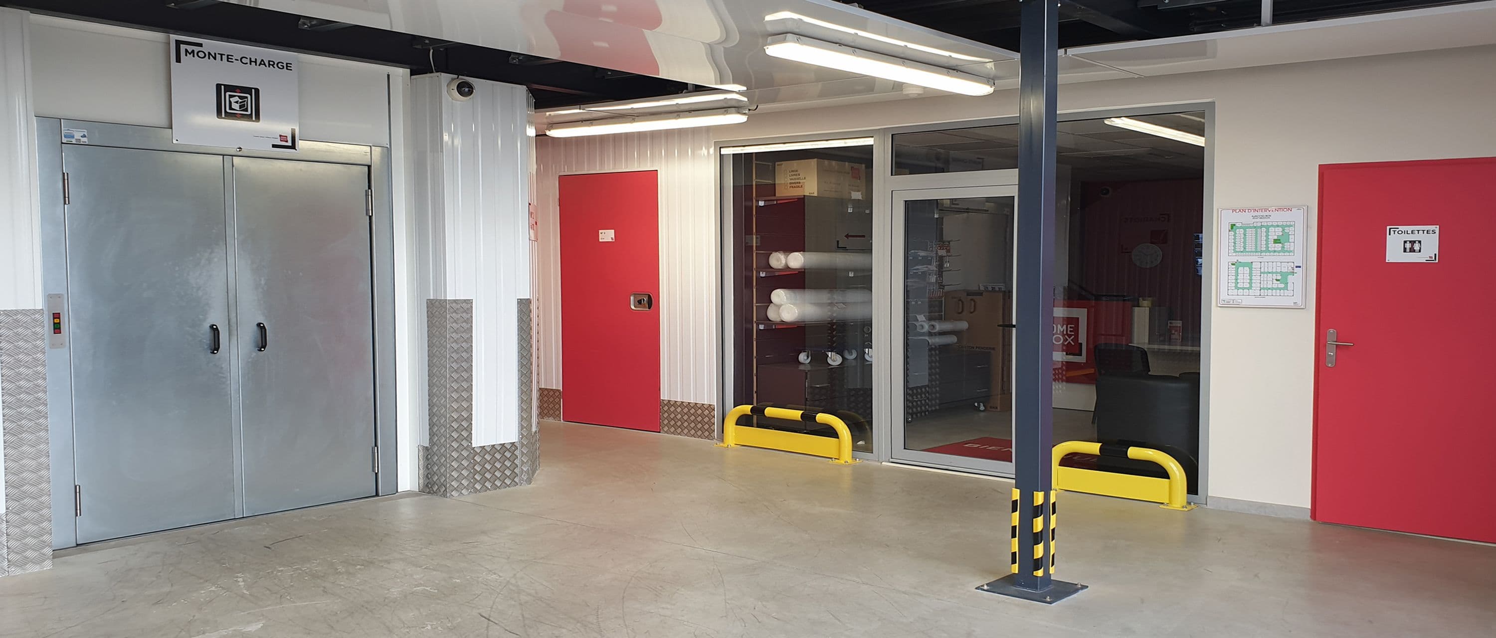Hall intérieur du centre HOMEBOX Ajaccio, situé à Mezzavia, avec ascenseur de service et portes rouges.