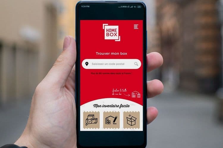 Main tenant un smartphone affichant l'application HOMEBOX 'Trouver mon box'
