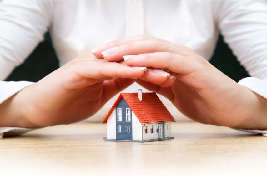 Mains protégeant une maison miniature symbolisant l'assurance habitation