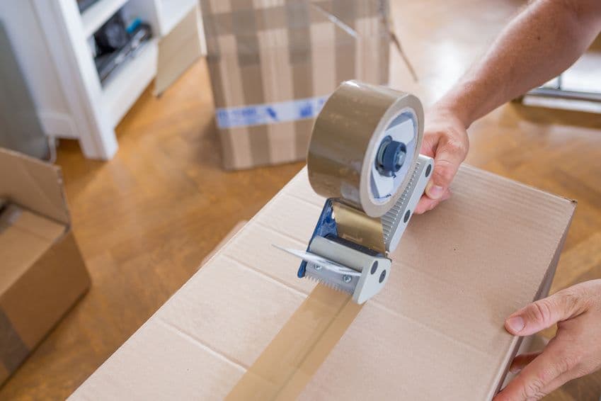 Mains scellant un carton de déménagement avec un dévidoir de ruban adhésif