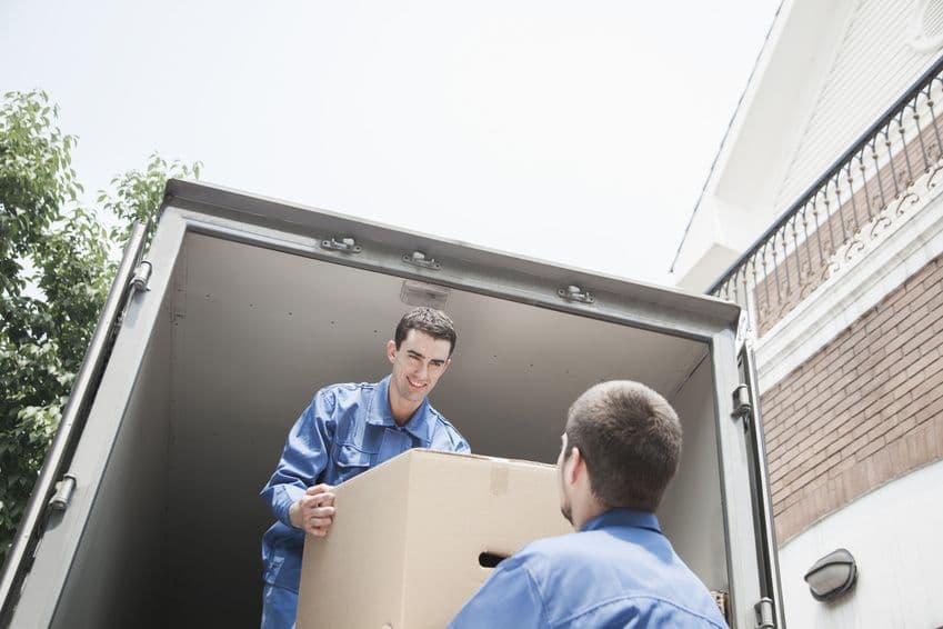 Deux déménageurs professionnels en uniforme bleu chargeant un carton dans un camion