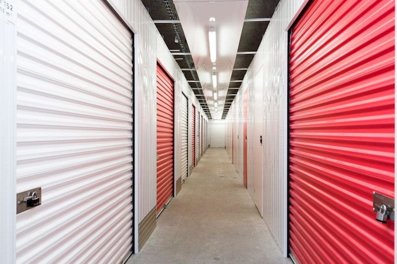 Long couloir intérieur entre rangées de portes de box rouges et blanches du centre HOMEBOX Roses