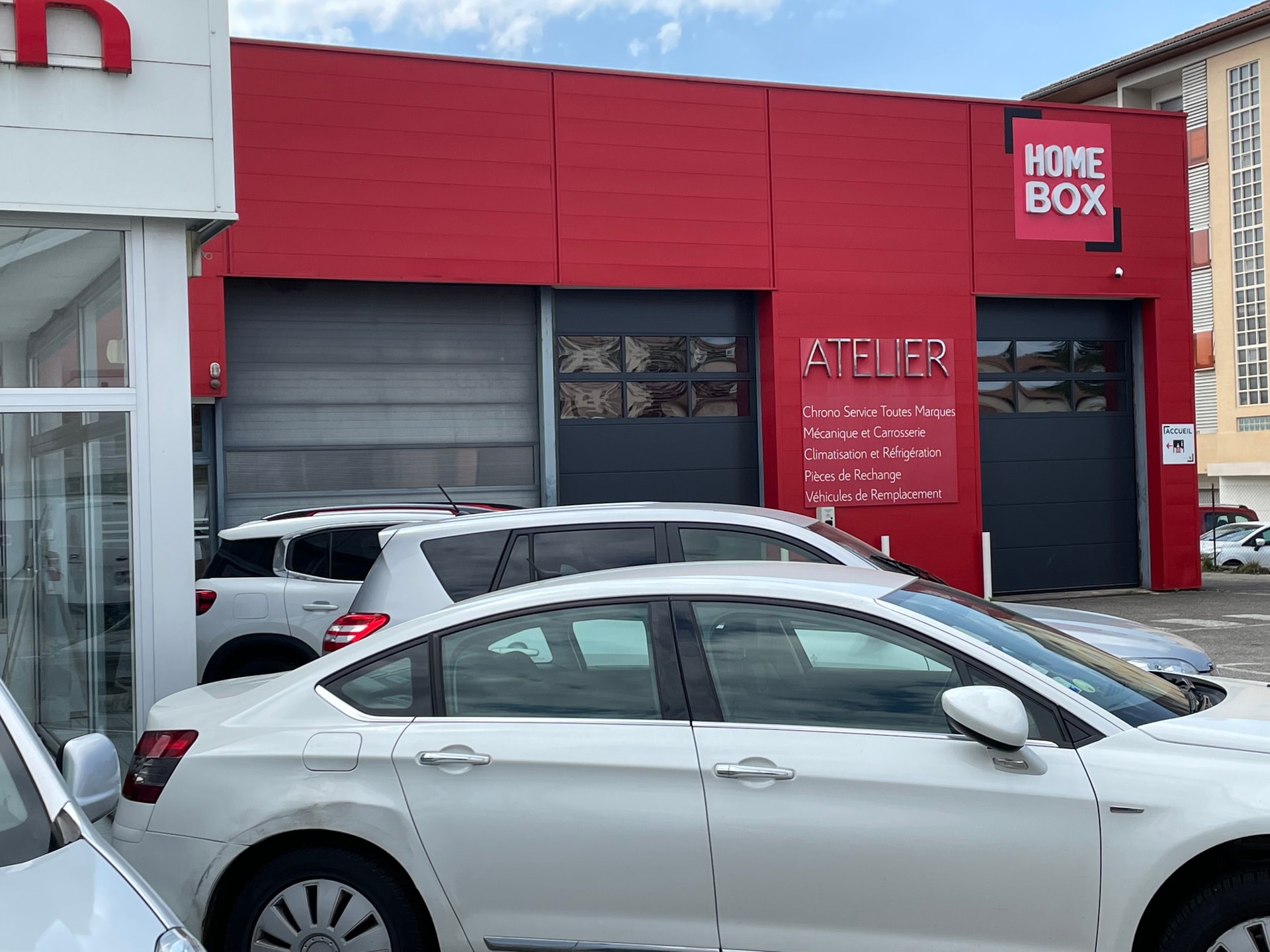 Façade rouge avec enseigne HOMEBOX au-dessus de l'atelier mécanique et véhicules stationnés, HOMEBOX Saint-Marcellin, 16 avenue des Alpes à Saint-Marcellin