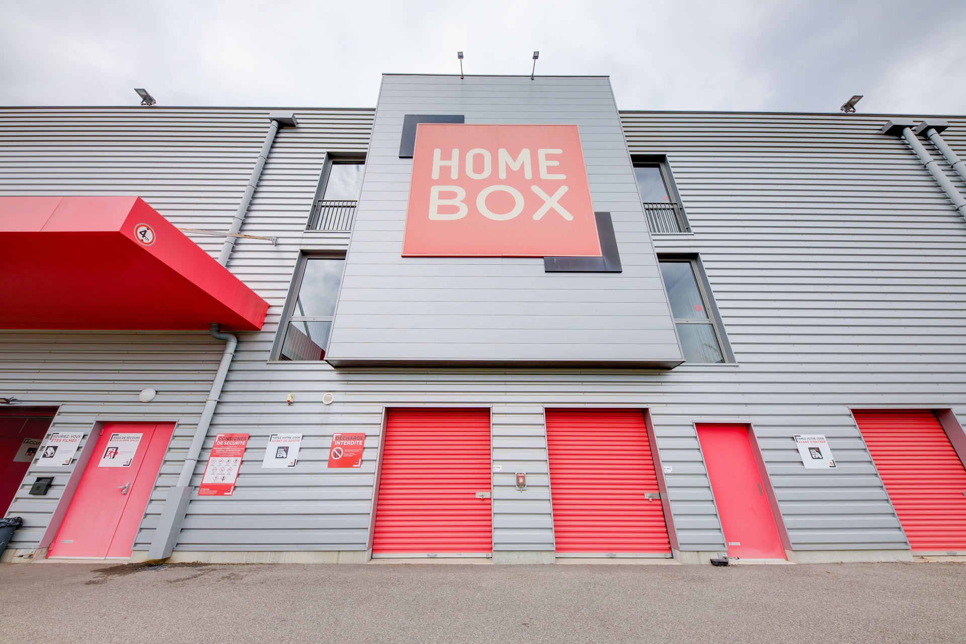 Façade grise avec grande enseigne HOMEBOX et portes de box rouges au rez-de-chaussée, HOMEBOX Mulhouse, 65 Rue de la rampe à Habsheim