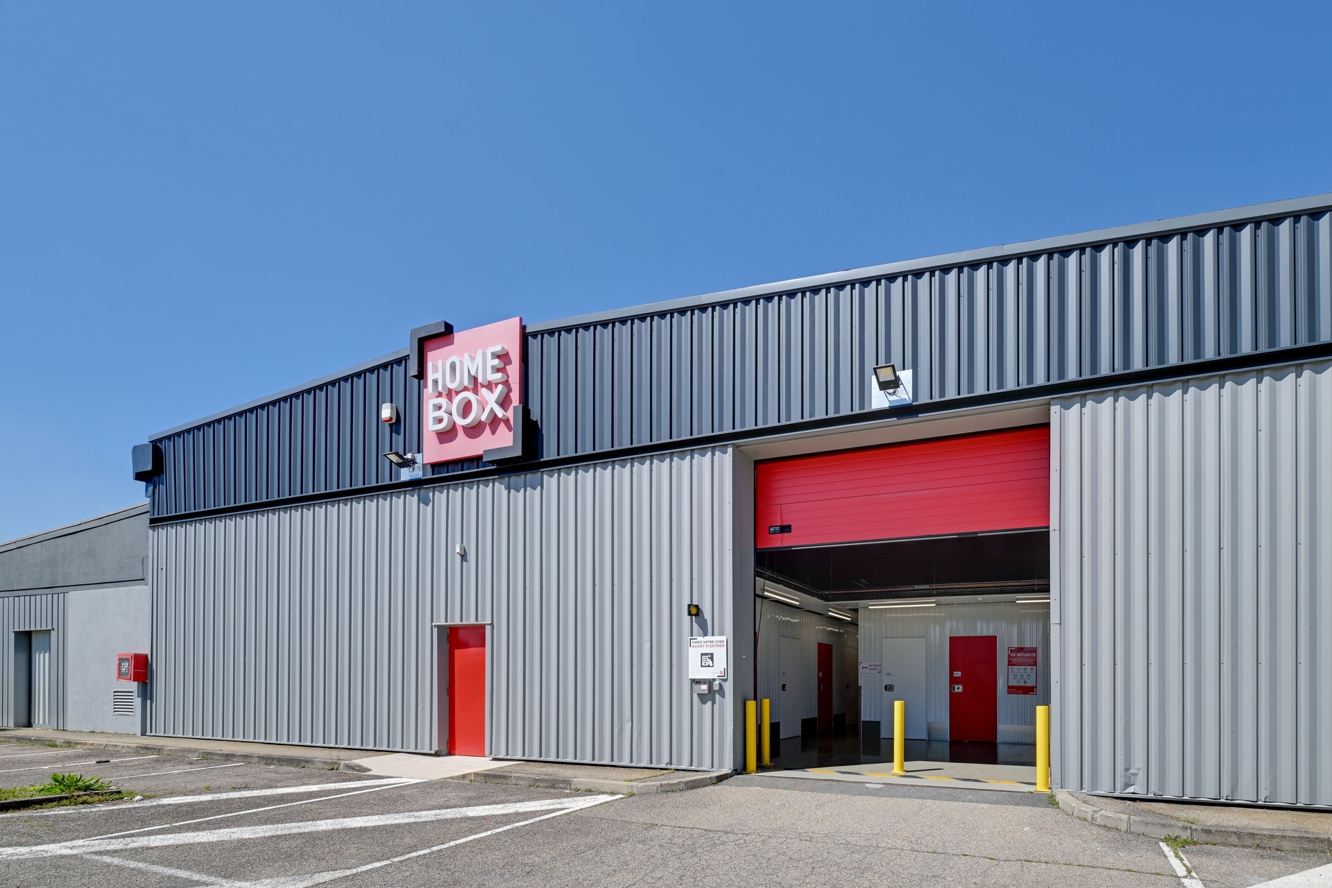 Façade grise avec enseigne lumineuse et porte d'accueil rouge, HOMEBOX Lyon Décines-Villeurbanne, 21 rue Emile Zola à Décines-Charpieu