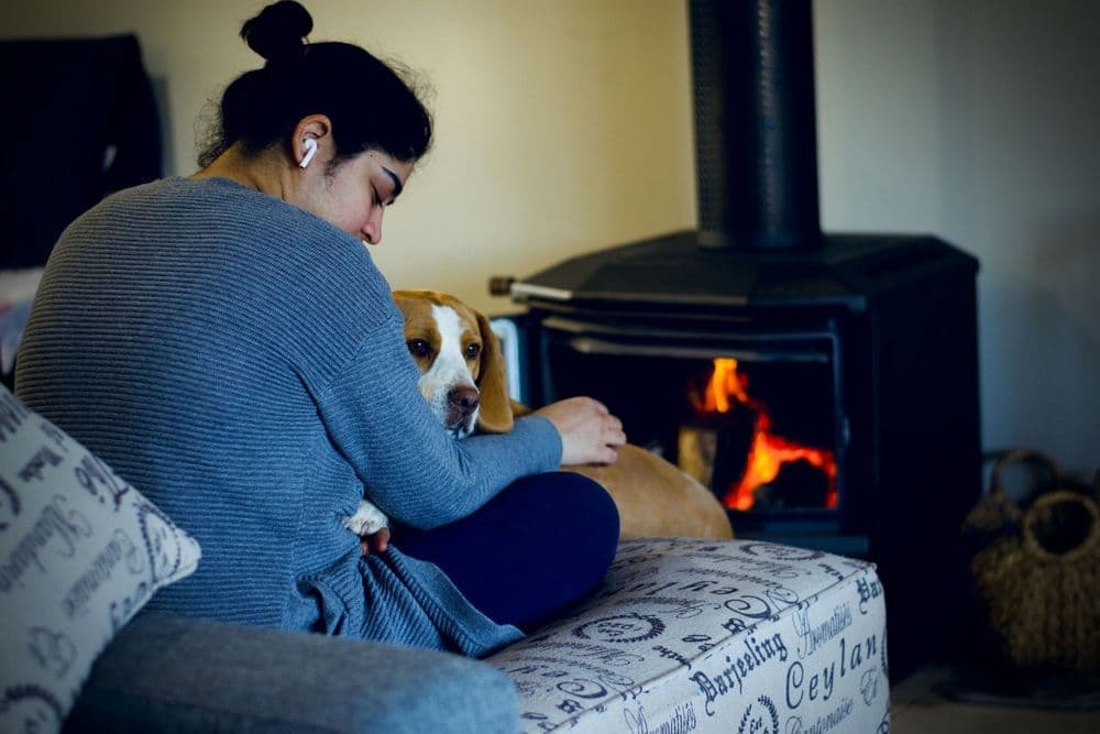 Personne sur un canapé avec son chien devant un poêle à bois