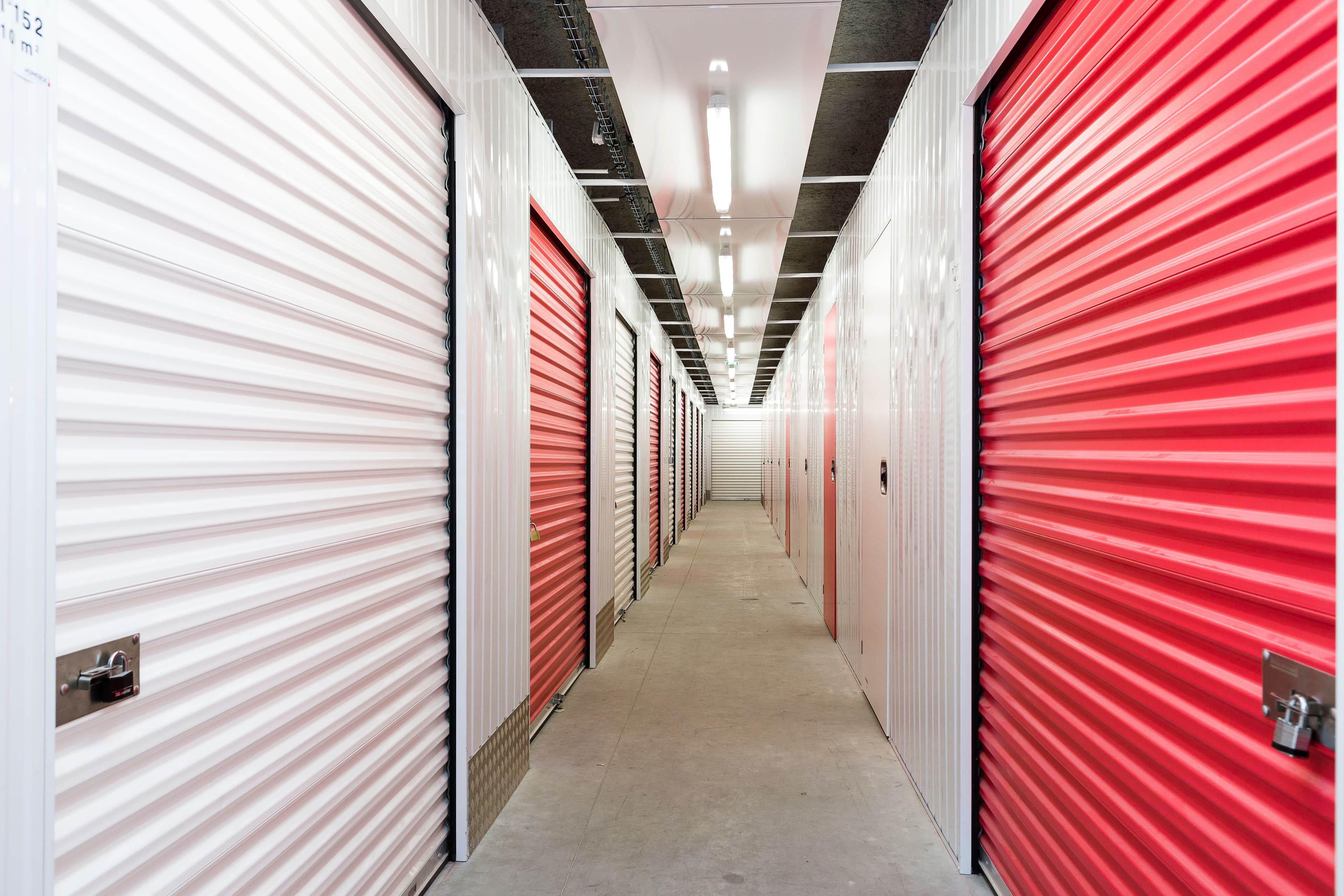 Couloir lumineux du centre HOMEBOX Angoulême La Couronne avec portes de box rouges et blanches.