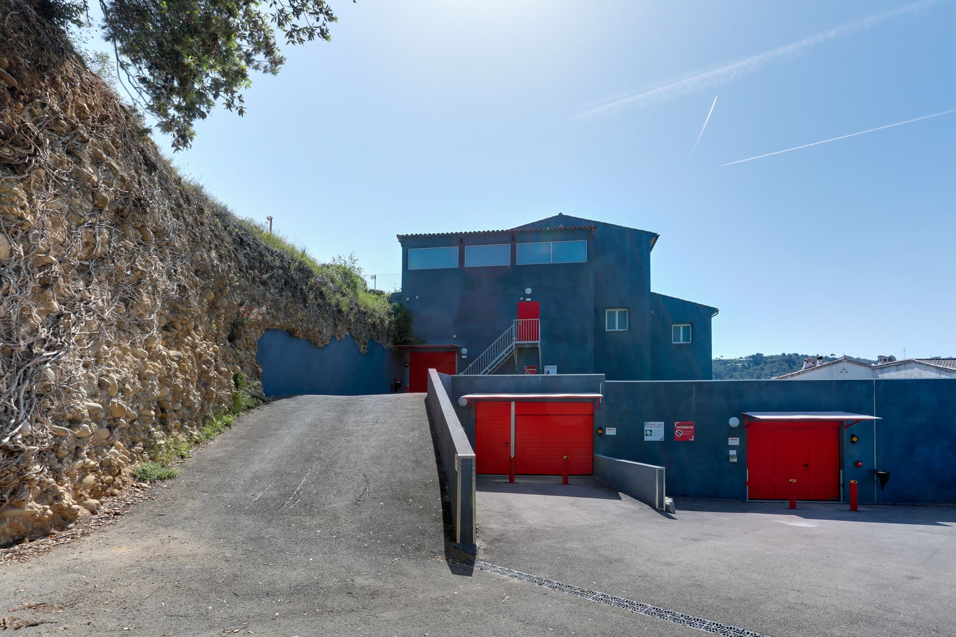 Bâtiment bleu adossé à une falaise avec rideaux rouges des box, HOMEBOX Nice-Carros, 650 route de la Baronne à Gattières