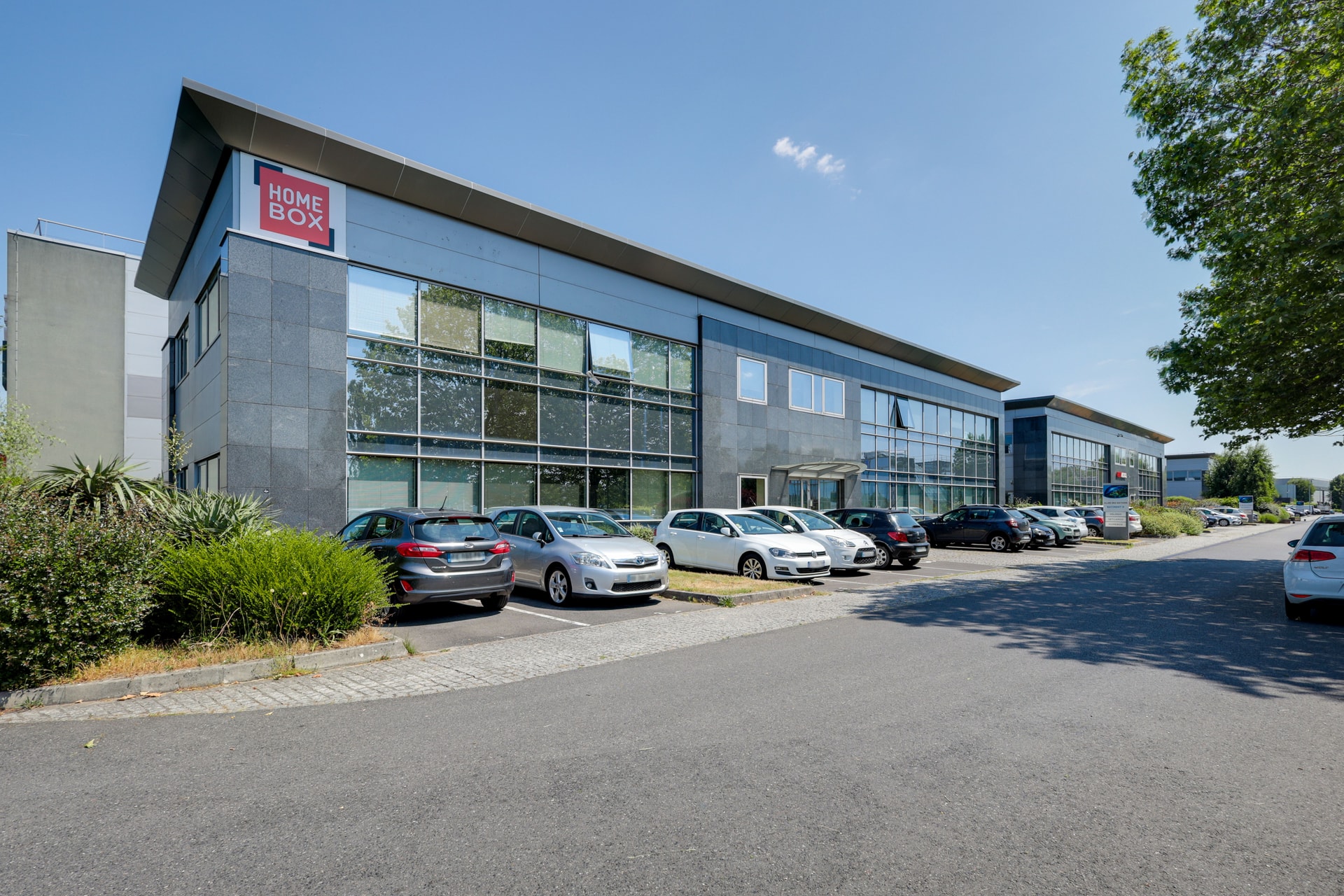 Bâtiment vitré moderne avec enseigne HOMEBOX et parking arboré, HOMEBOX Roissy, 383 rue de la Belle Etoile Parc des Nations à Roissy