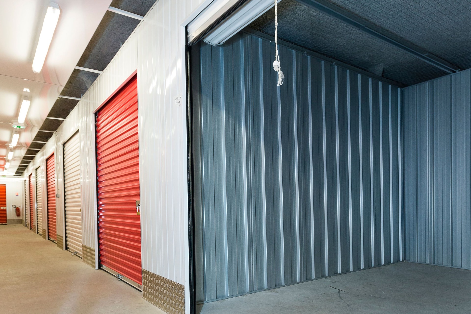 Couloir intérieur avec portes de box rouges fermées et grand box ouvert aux parois métalliques du centre HOMEBOX Madrid Atocha
