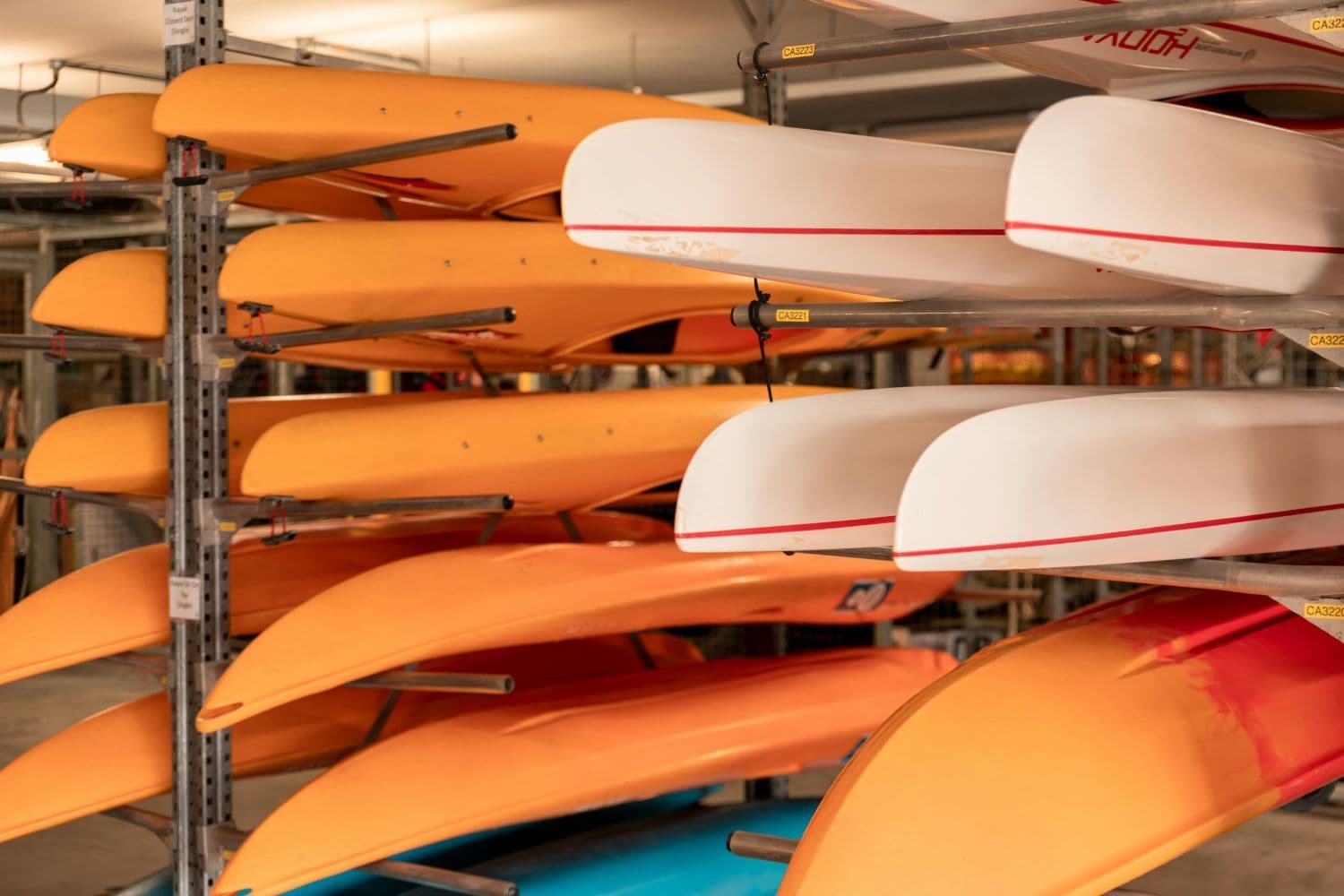 Kayaks blancs et oranges superposés sur des racks en intérieur
