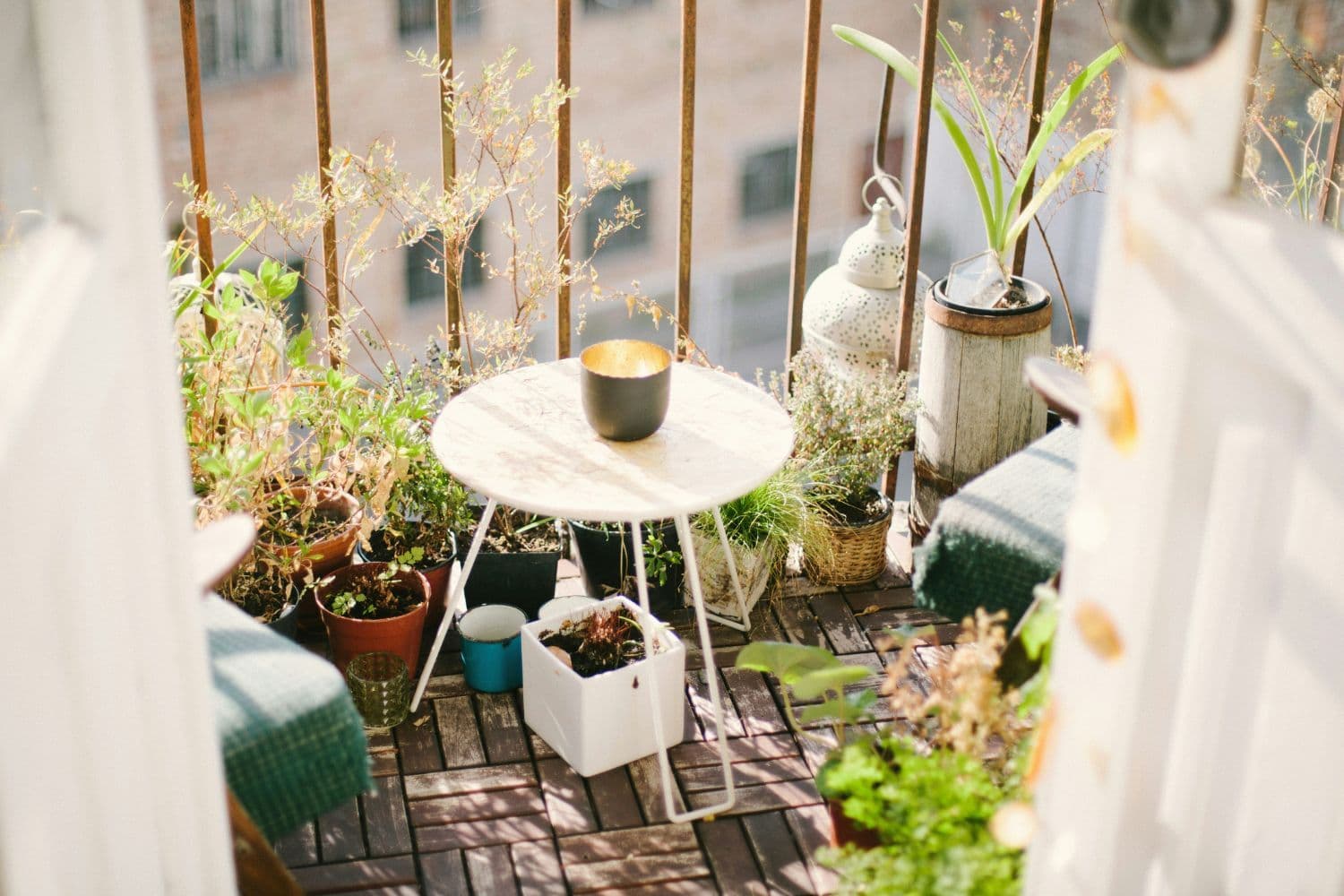 Vue sur un petit balcon équipé de caillebotis, d’une table blanche en métal et de plantes