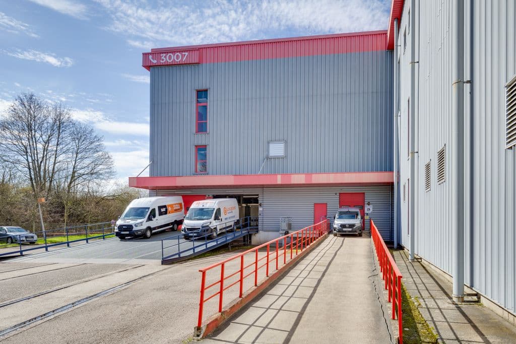 Bâtiment de stockage gris et rouge avec rampe d'accès et utilitaires stationnés devant les quais, HOMEBOX Metz, 37, avenue des Deux Fontaines à Metz
