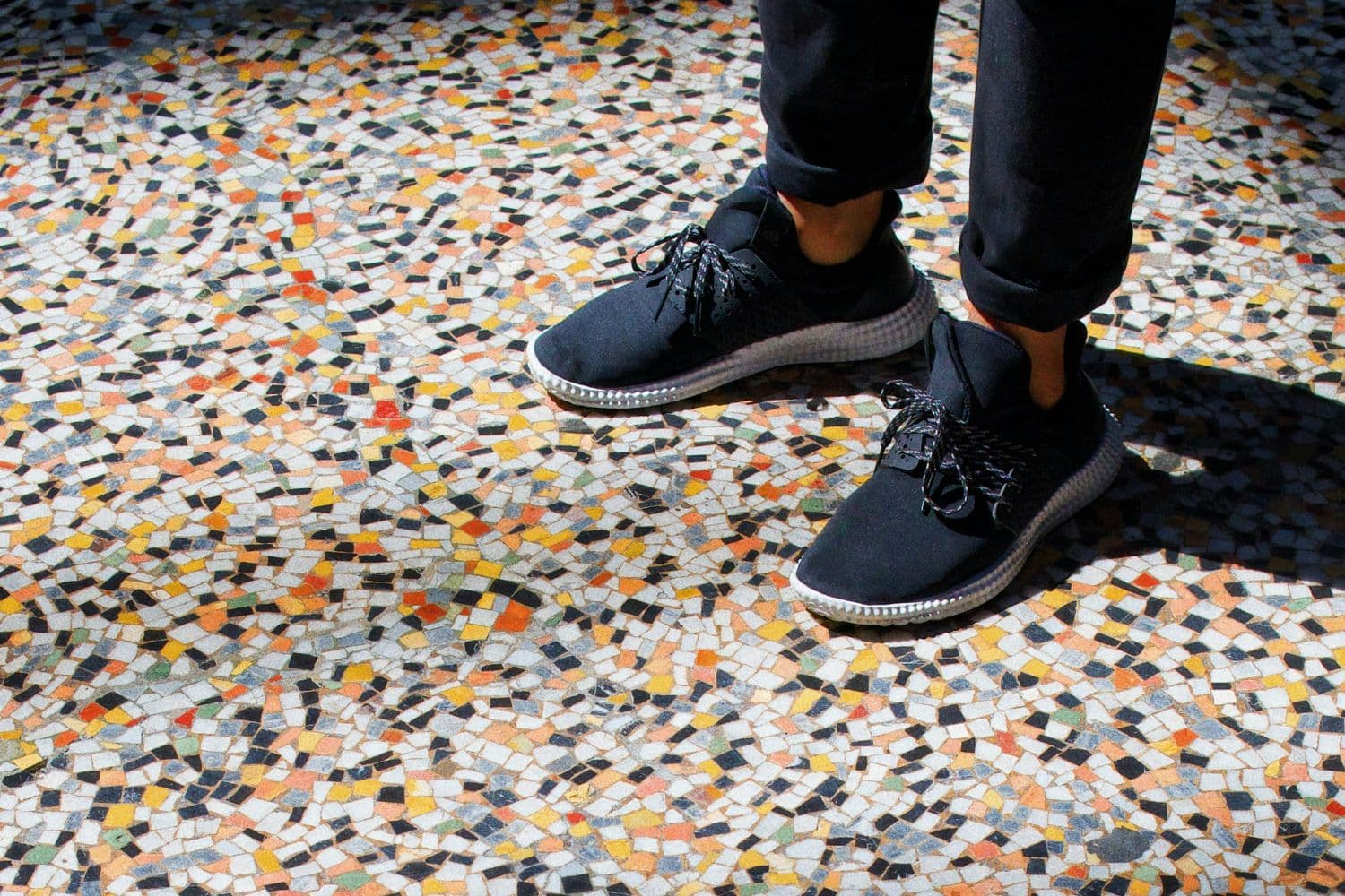 Personne en baskets bleues et jean sur un carrelage en mosaïque multicolore