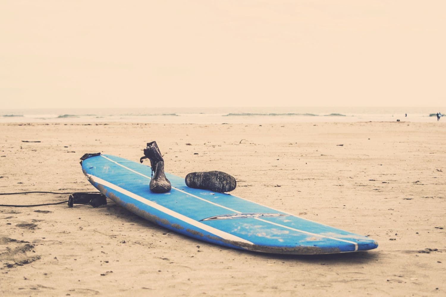 Planche de surf sur une plage accompagnée de chaussures de surf, temps gris