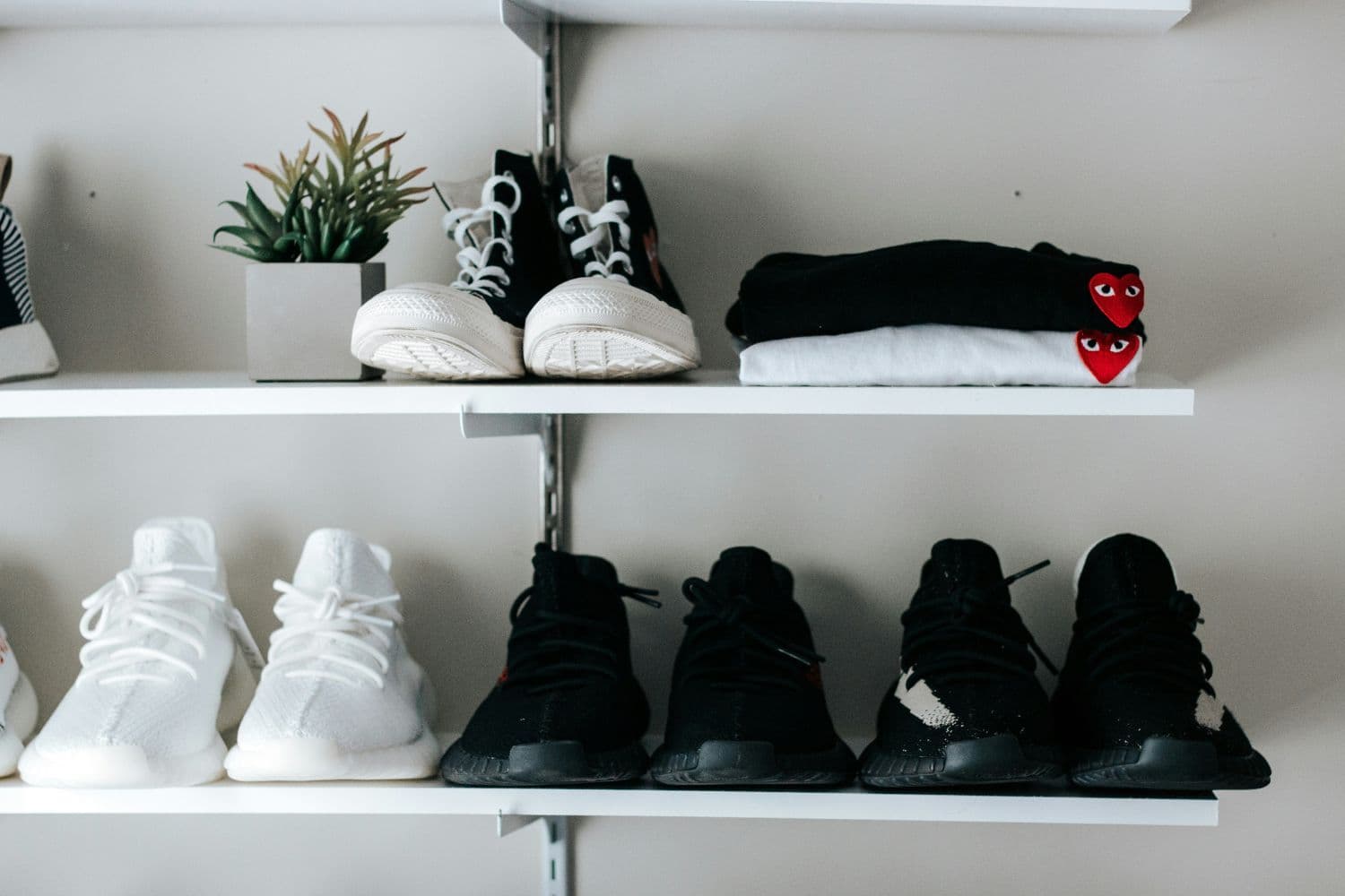 Quatre paires de chaussures sur des étagères murales blanches avec des t-shirts