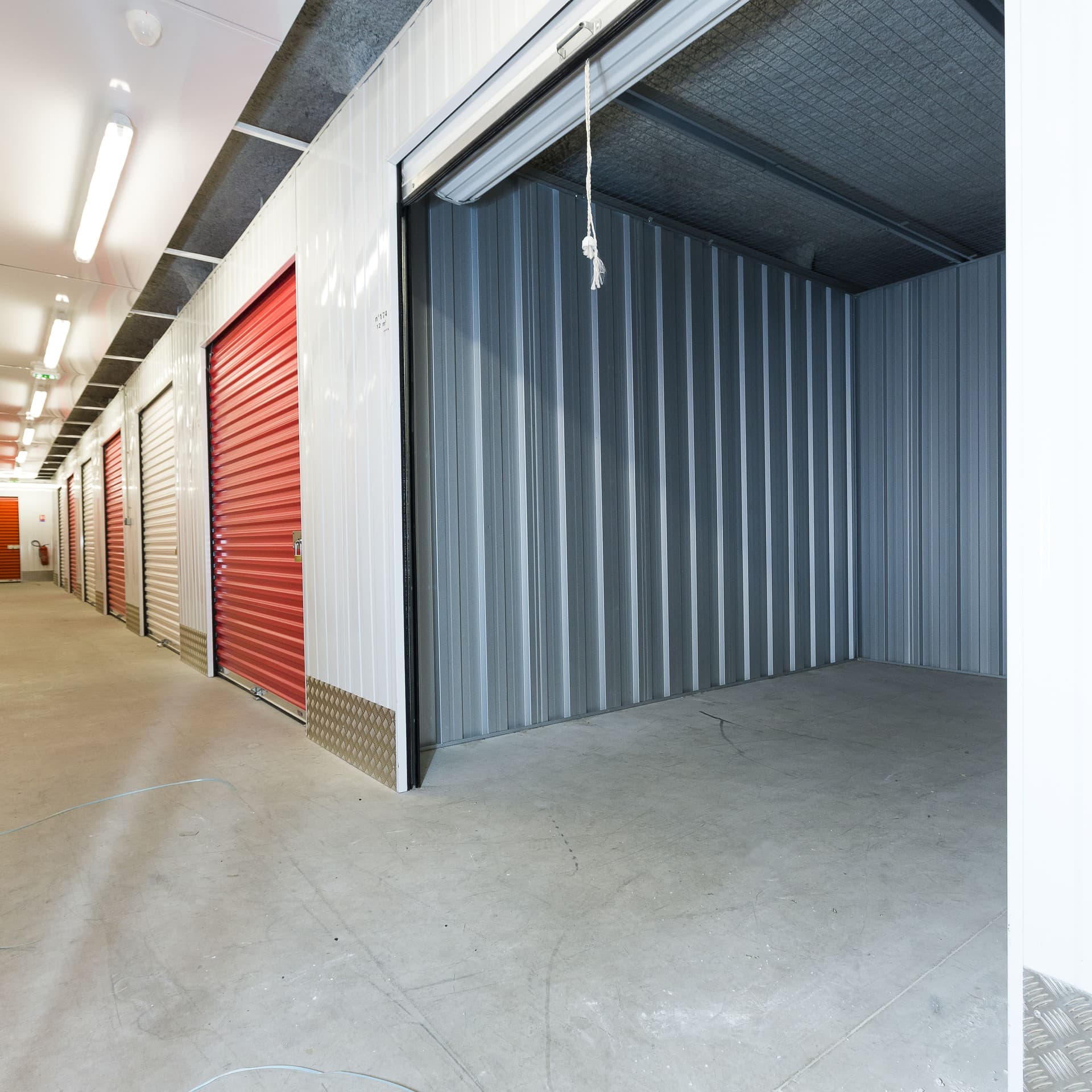 Box de stockage ouvert avec porte rouge et couloir éclairé du centre HOMEBOX Les Sables d'Olonne