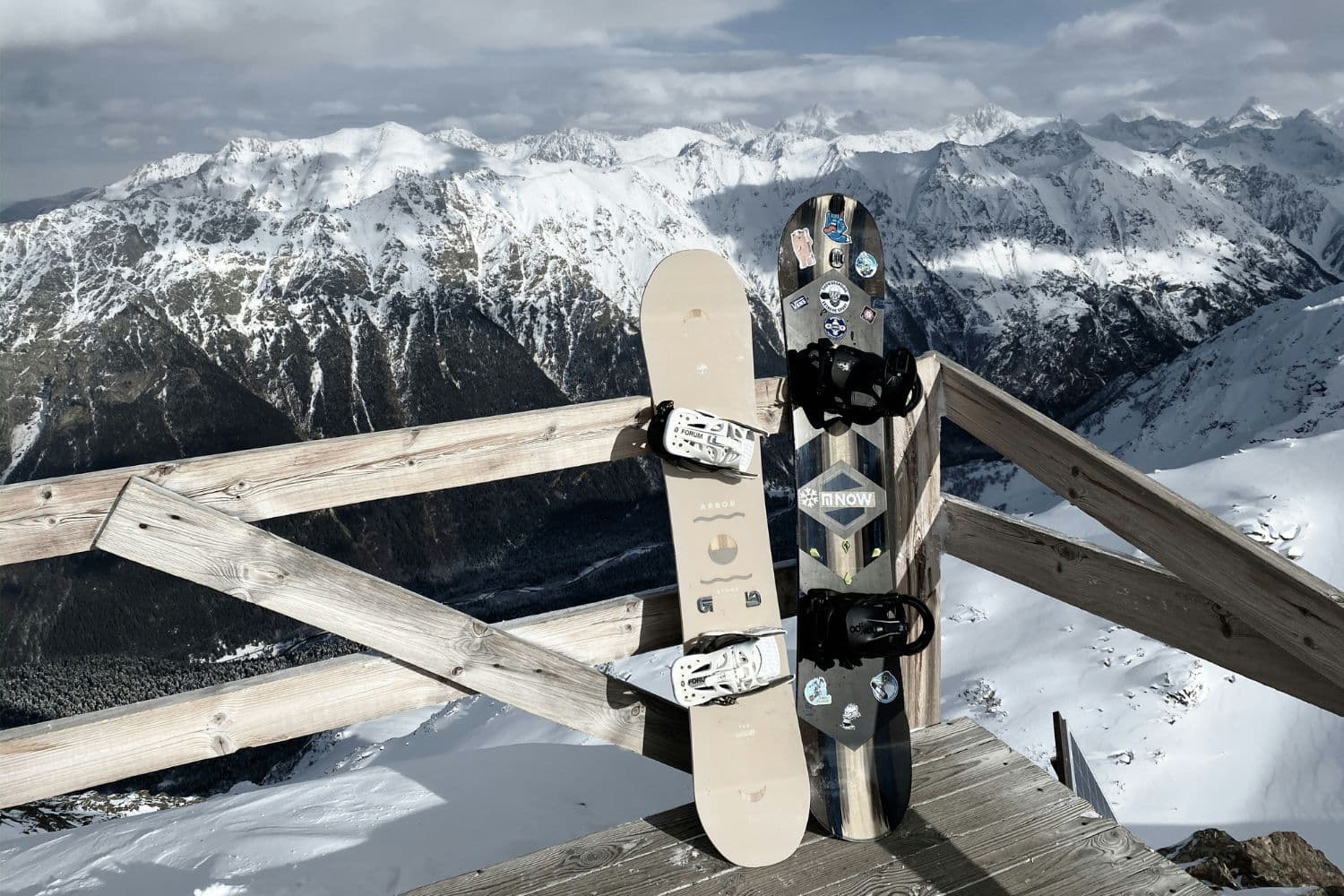 Deux planches de snowboard posées contre des rambardes en bois face à une chaîne de montagnes