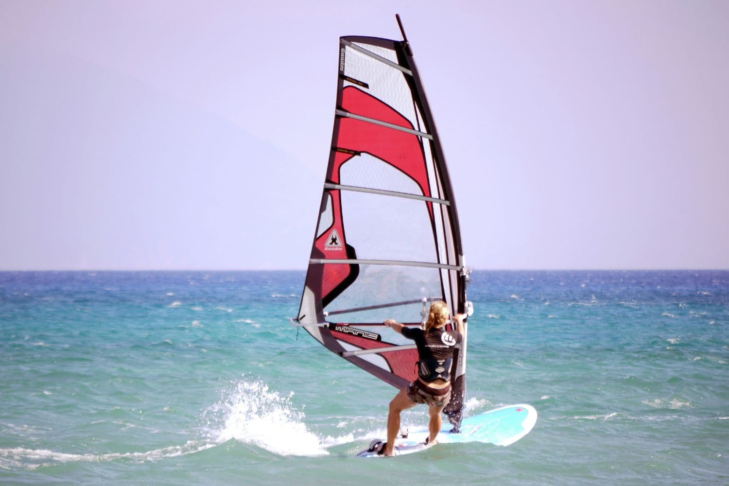 Personne de dos faisant de la planche à voile en pleine mer
