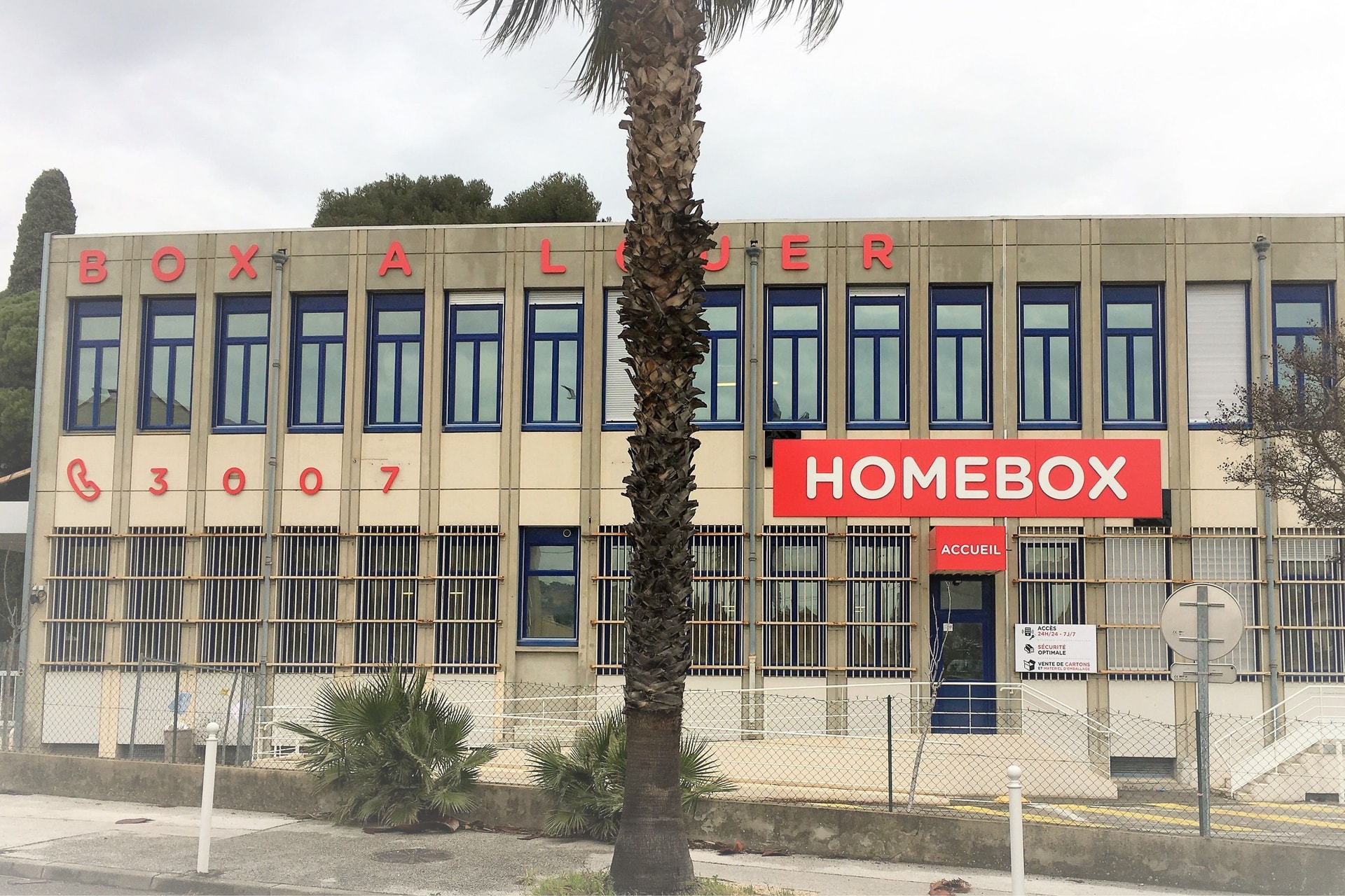 Façade beige avec enseigne rouge accueil et palmier, HOMEBOX Toulon - Les Routes, 264 Avenue André le Chatelier à Toulon