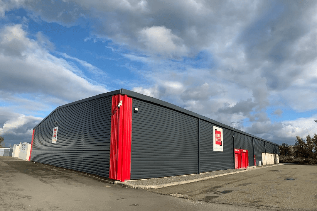Façade extérieure noire avec portails rouges sous ciel nuageux, HOMEBOX Le Mans, 95 route du chêne à Arnage