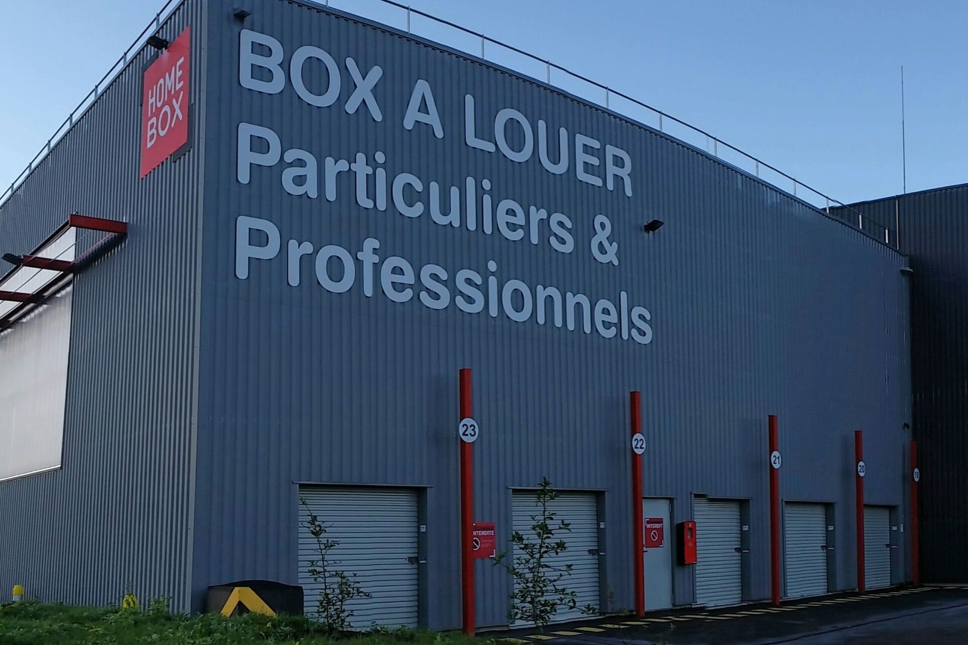 Vue extérieure de la façade avec enseigne HOMEBOX et portes roulantes grises, HOMEBOX Carrières-Chanteloup, 5 rue Henri Navier à Chanteloup-Les-Vignes
