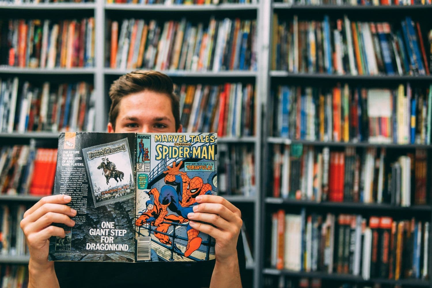 Personne lisant un comics Spiderman devant une grande bibliothèque