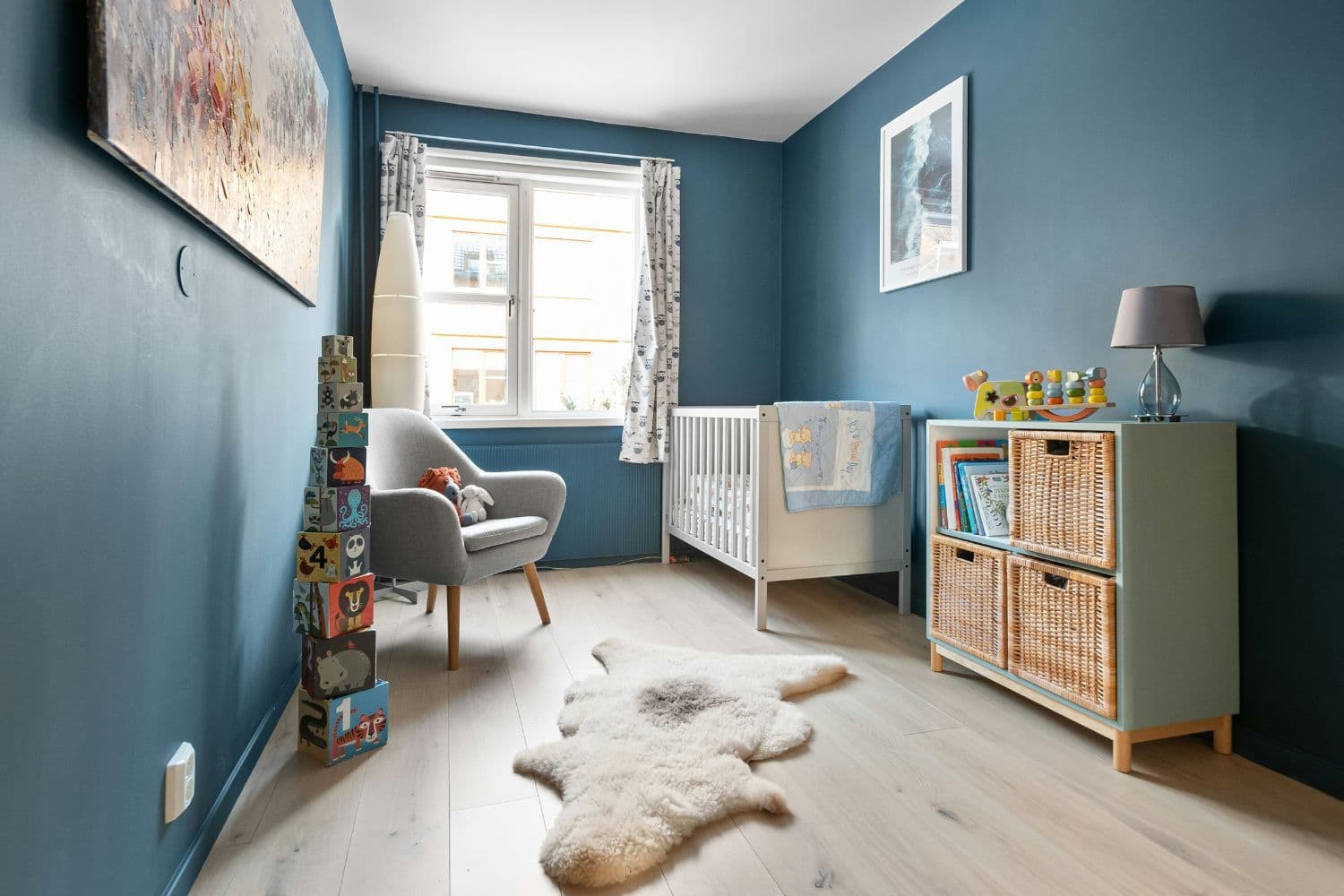 Chambre de bébé avec commode à paniers en osier, tapis fausse fourrure au sol et murs bleus