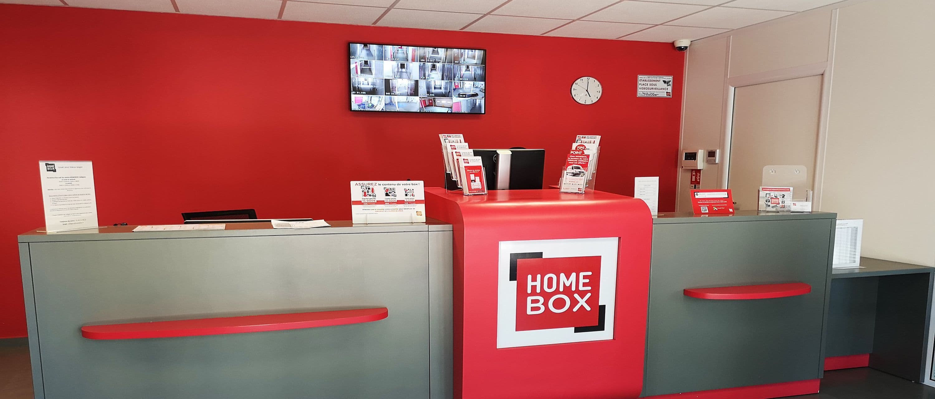 Accueil avec comptoir rouge et gris et écran de vidéosurveillance au centre HOMEBOX Cholet.