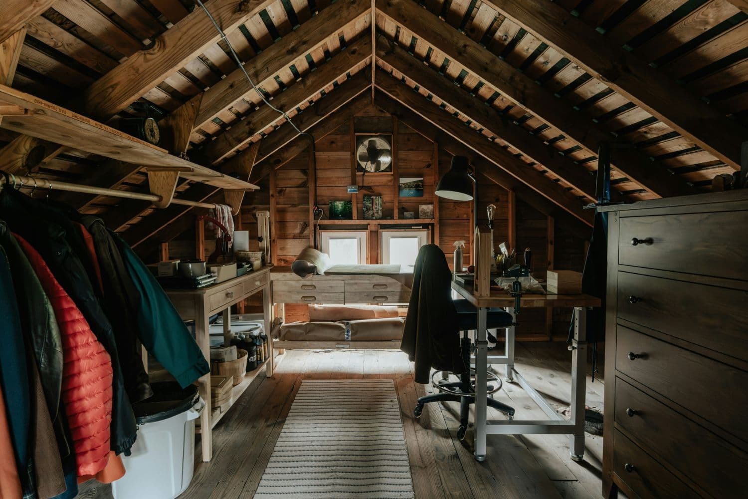 Combles aménagés avec des portants et vêtements à gauche, une commode et un bureau à droite et dans le fond