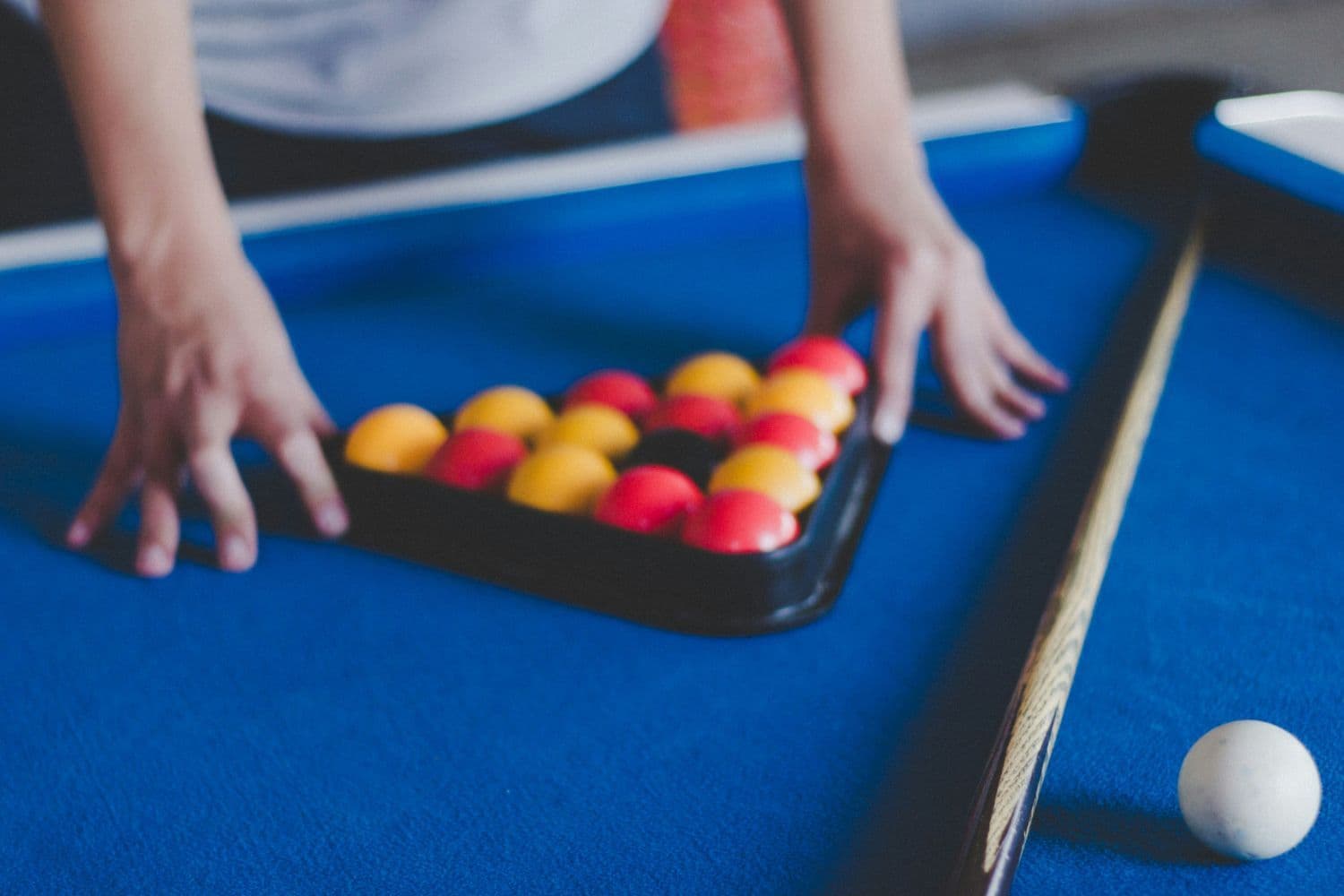 Mains d’une personne tenant un triangle rempli de billes rouges et jaunes, queue de billard posée sur le côté