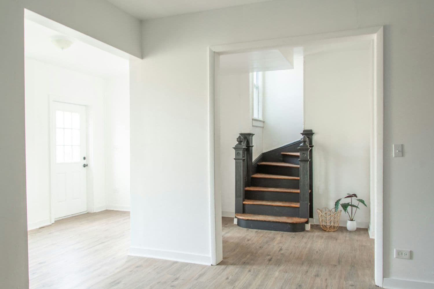 Vue sur les pièces vides d’une maison aux murs blancs, escalier ancien en bois au second plan