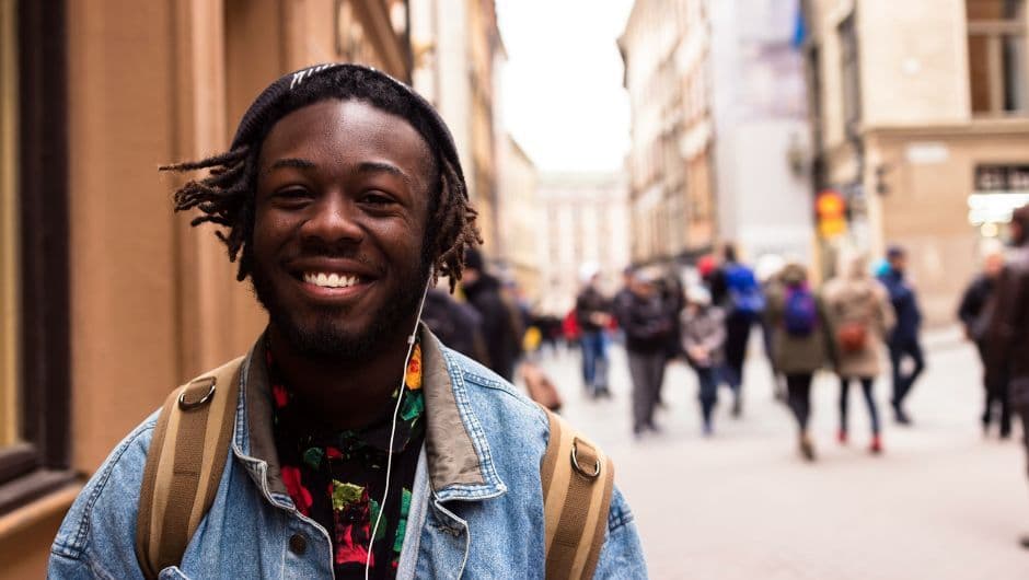 Gros plan sur un jeune étudiant souriant dans la rue, veste en jean, écouteurs et chemise à motifs colorés