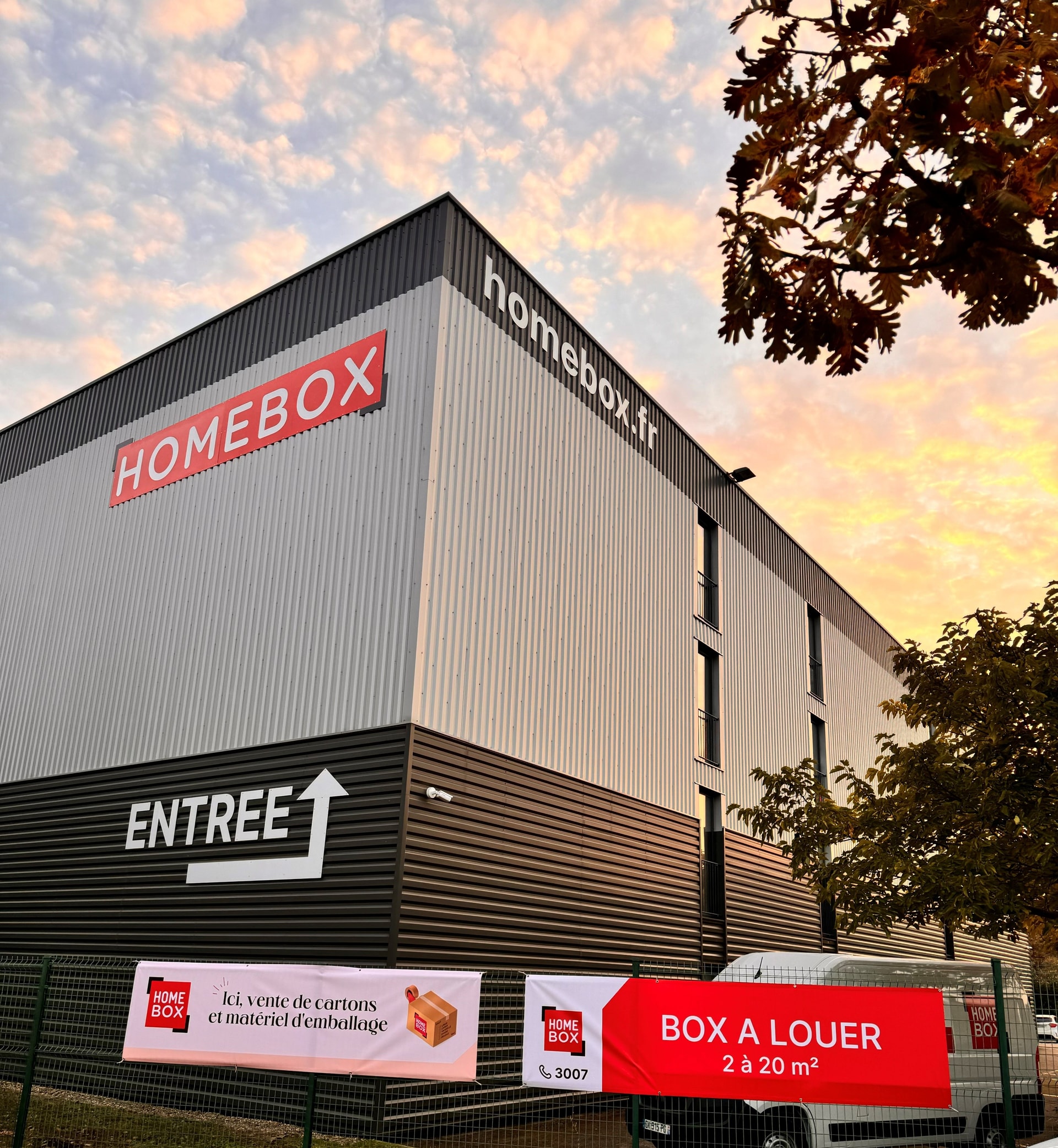Façade avec enseigne lumineuse et signalétique entrée au coucher du soleil, HOMEBOX Lyon Craponne, 225 avenue Pierre Auguste Roiret à Craponne