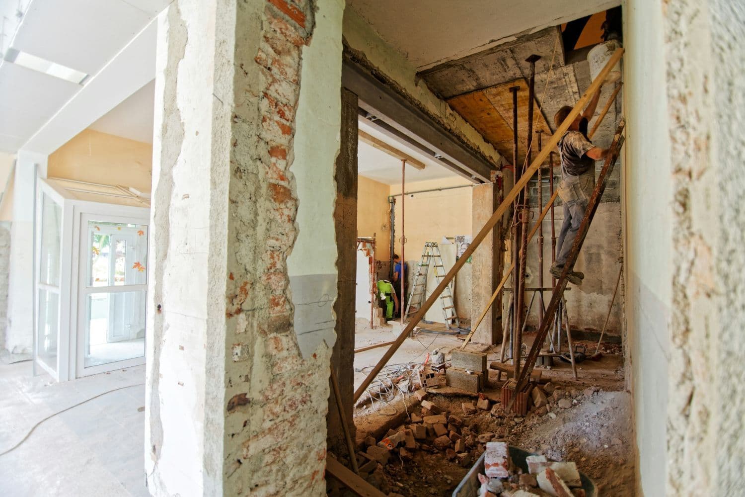 Vastes travaux à l’intérieur d’une pièce en rez-de-chaussée. Homme sur une échelle à droite