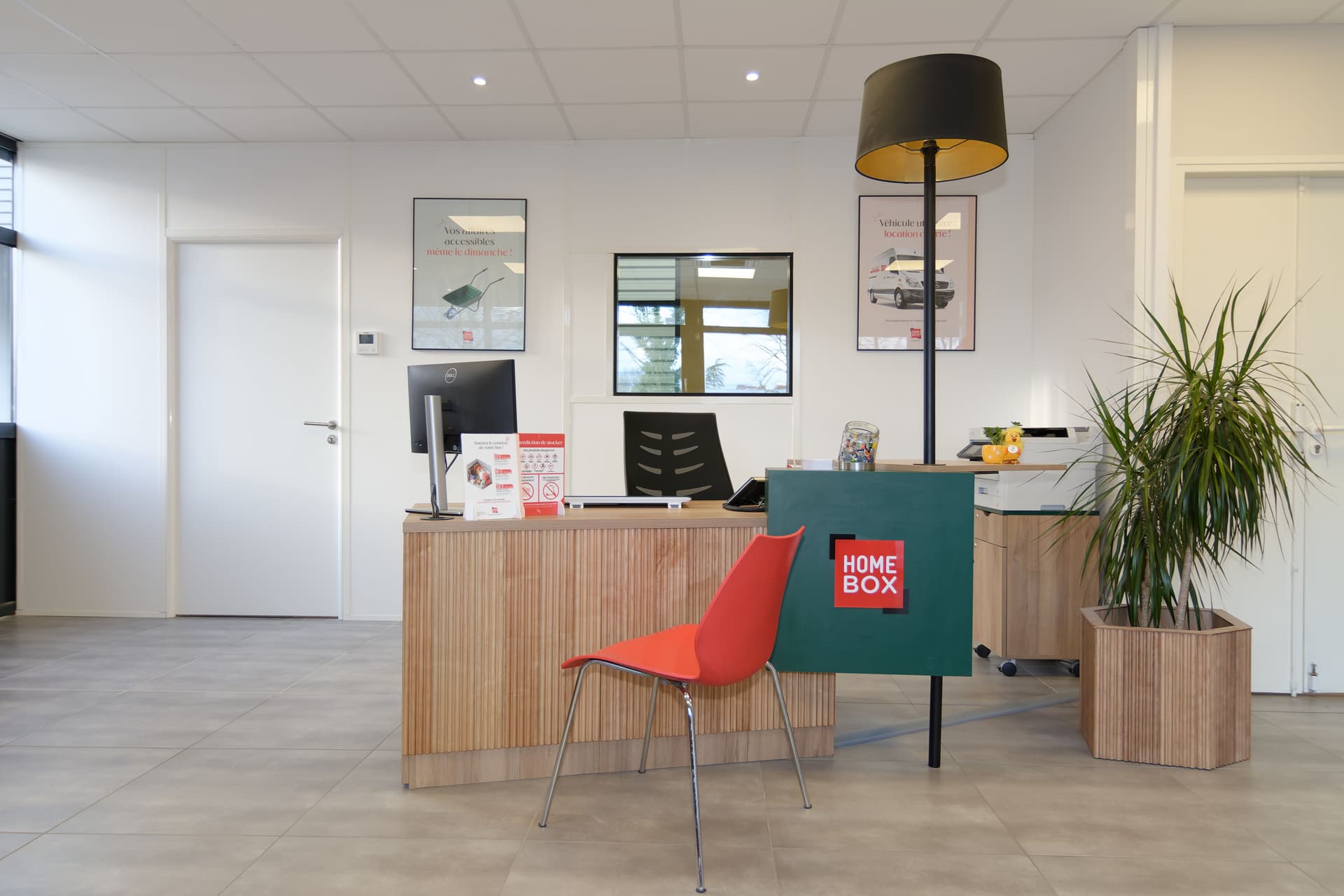 Espace d'accueil bois et blanc avec comptoir HOMEBOX, chaise rouge et plante verte du centre HOMEBOX Nantes
