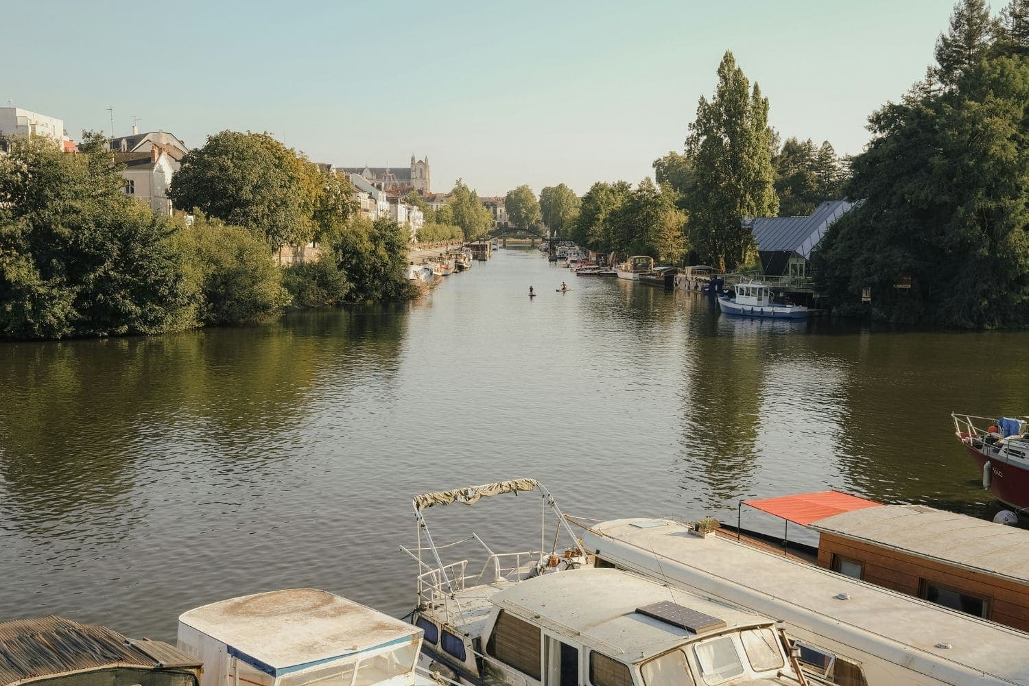 Péniches et bateaux de plaisance au premier plan, Erdre bordée d’arbres au second en fin de journée